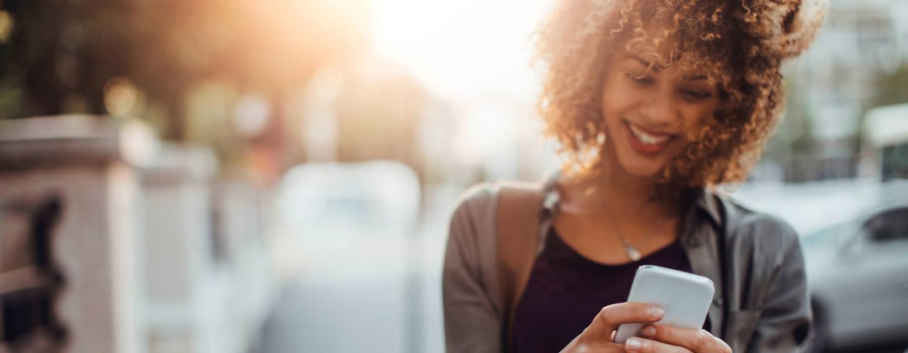 woman texts on her phone as she walks through the city