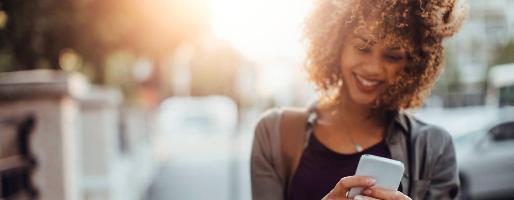 woman texts on her phone as she walks through the city